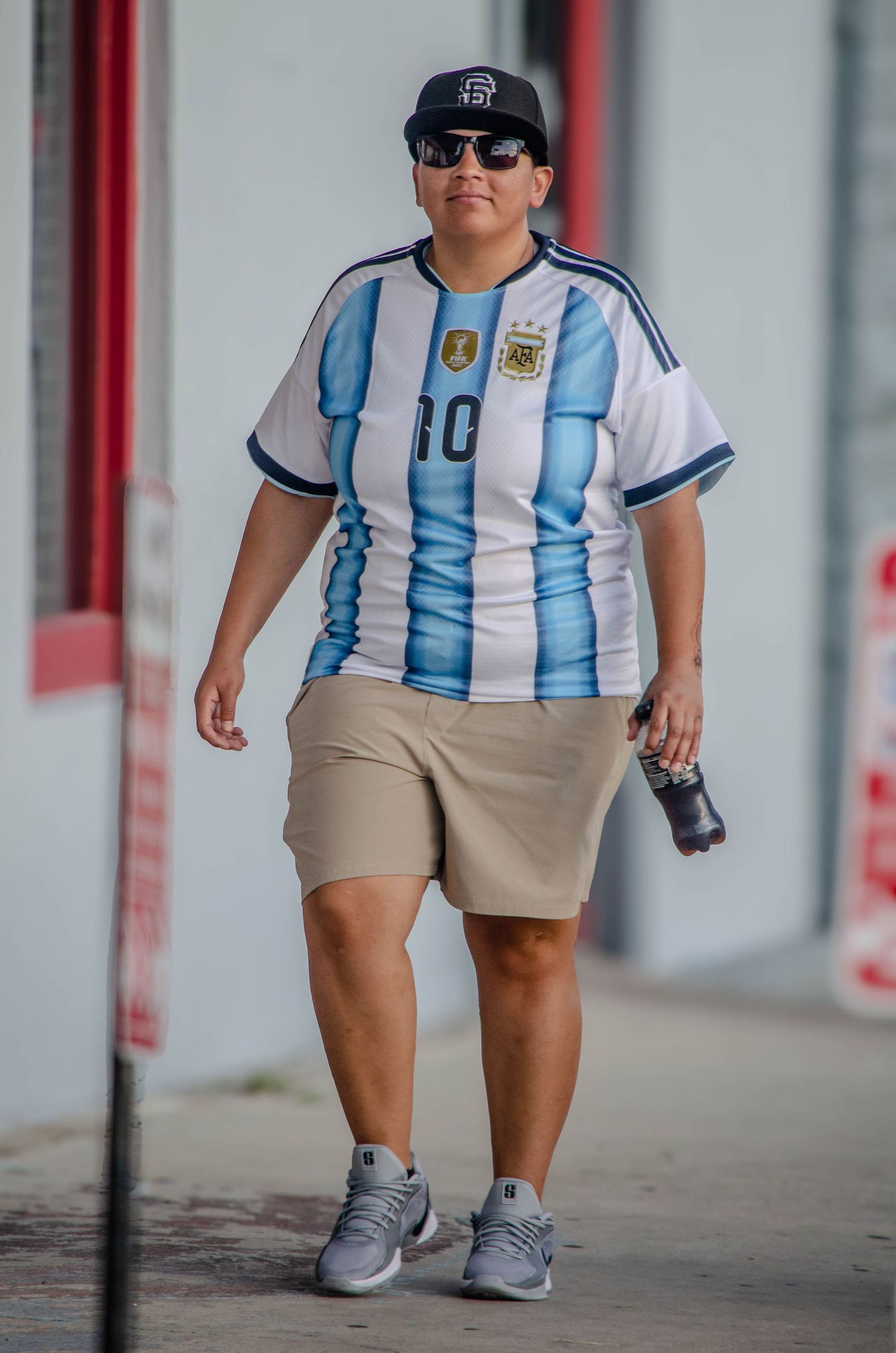 Person wearing Argentina number 10 soccer jersey, cap, and shorts walking outdoors.