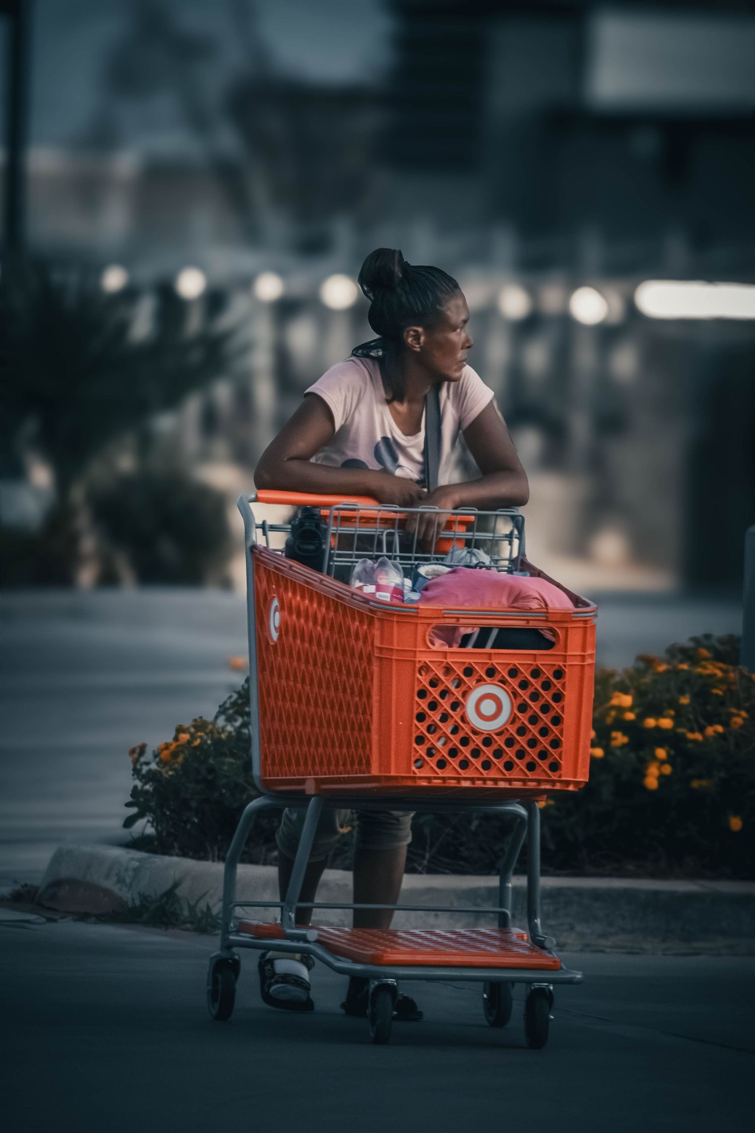 Woman pushing a red Target shopping cart in a parking lot, with flowers and a blurred building in the background.