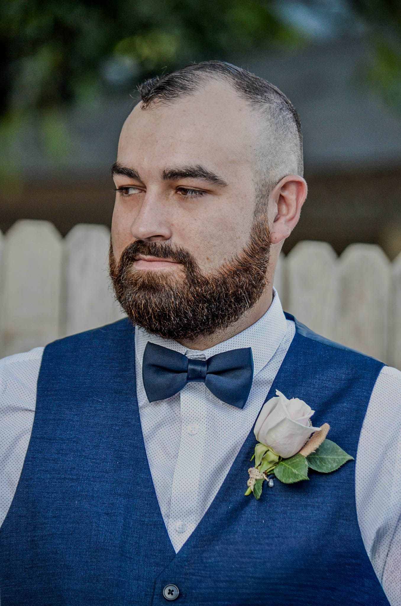 Bearded man in blue vest and bow tie with boutonniere at a wedding.