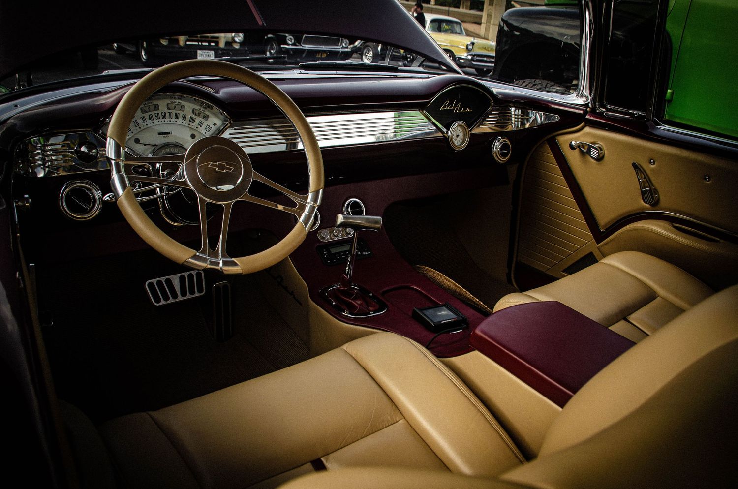 Vintage car interior with wood steering wheel, tan leather seats, and classic dashboard gauges.