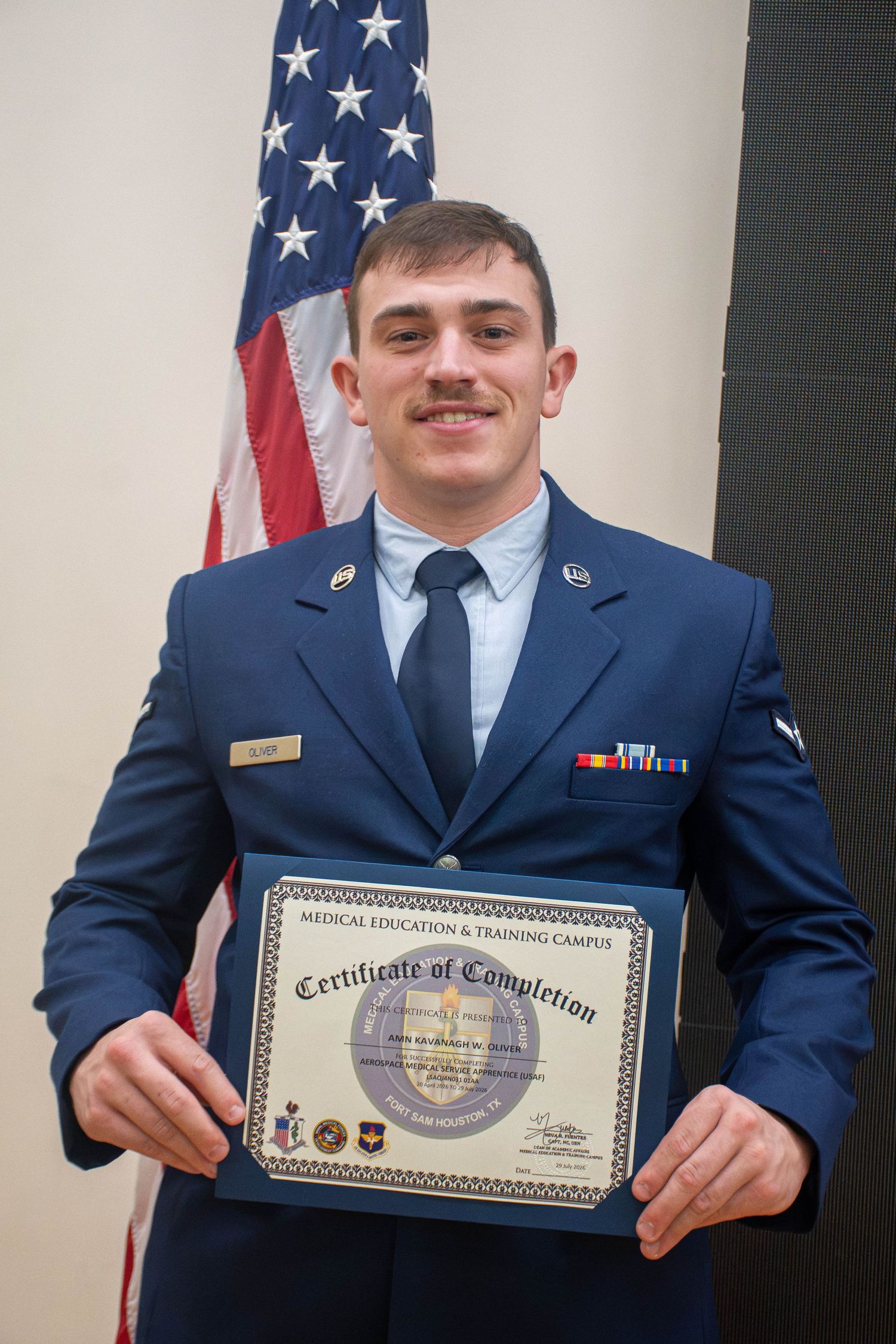 Smiling US Air Force airman in dress blues holding a Medical Education and Training Campus certificate.