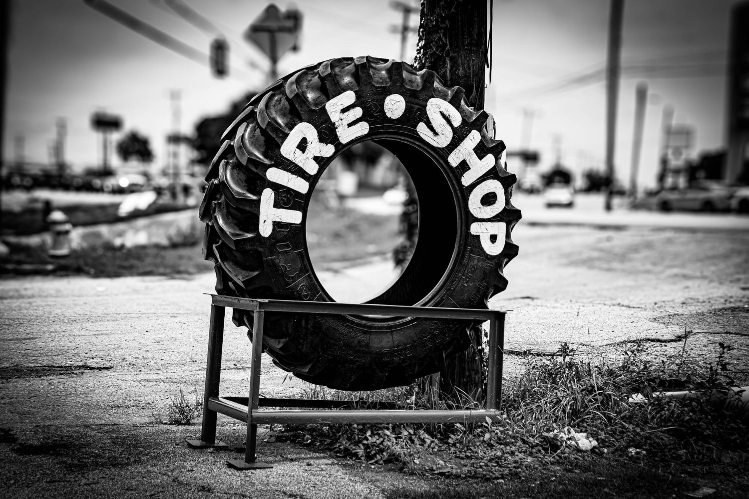 Vintage black and white photo of a large tire sign reading Tire Shop on a roadside stand.