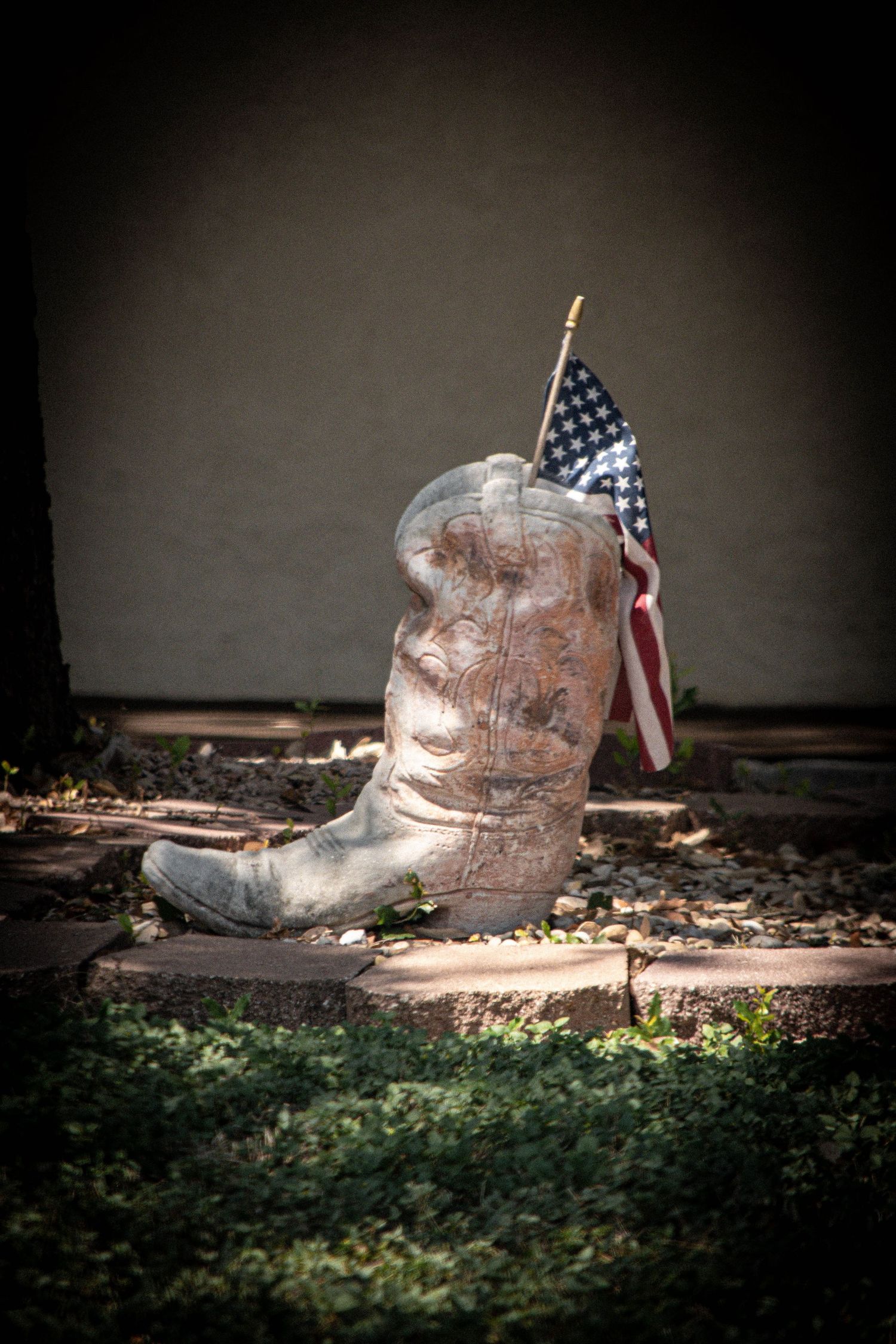 Worn cowboy boot with American flag displayed outdoors on stone path against stucco wall.