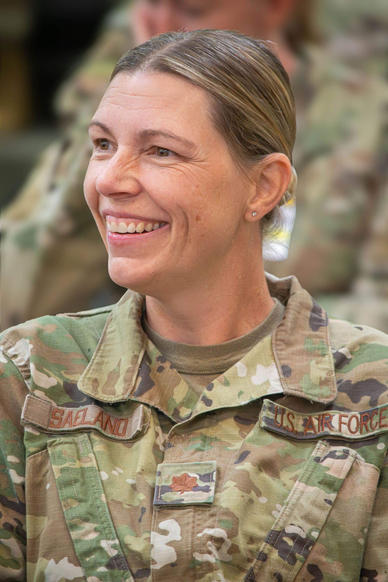 Smiling US Air Force female officer in OCP camouflage uniform with name tape Saeland and oak leaf insignia.