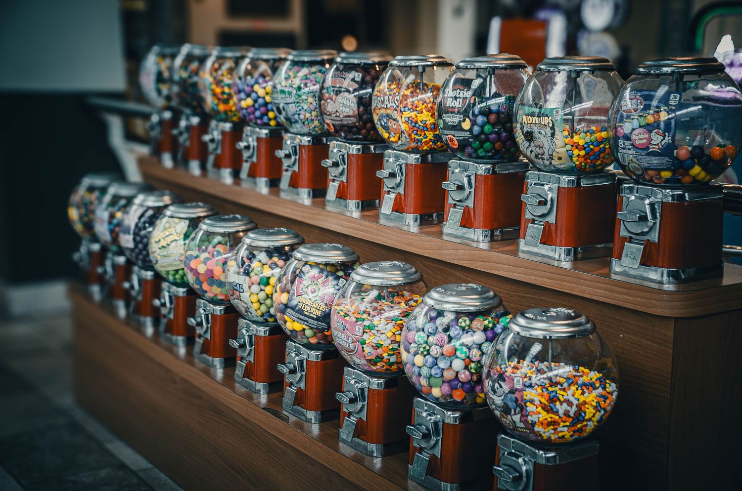 Rows of colorful gumball candy vending machines displayed on wooden shelves in a store.