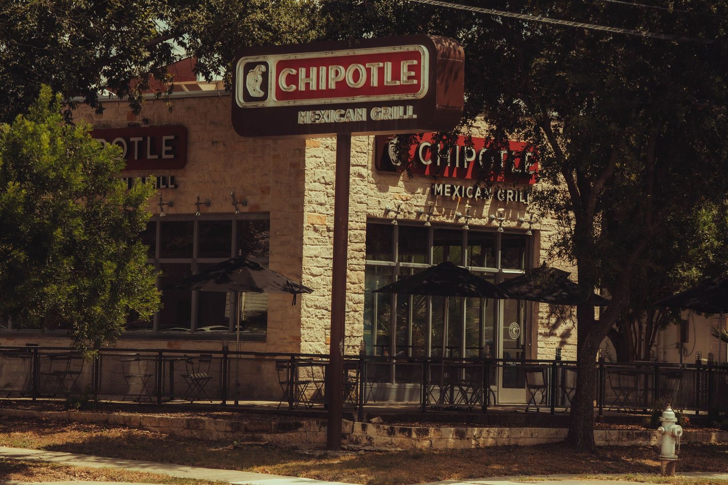 Vintage-style Chipotle Mexican Grill restaurant in a stone building surrounded by large trees.