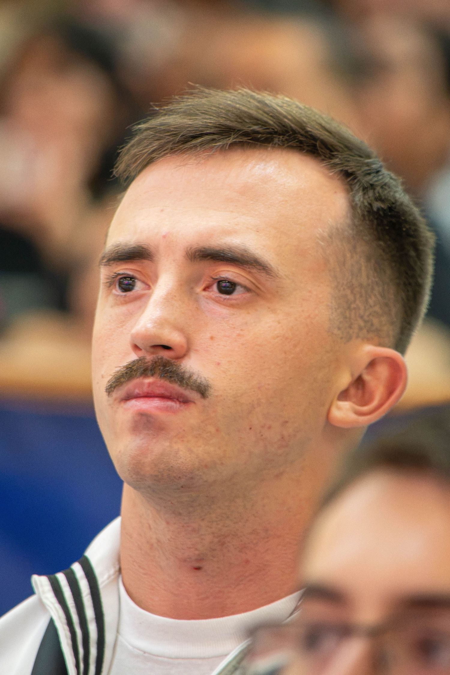 Young male Navy sailor with mustache in white uniform at military graduation ceremony.