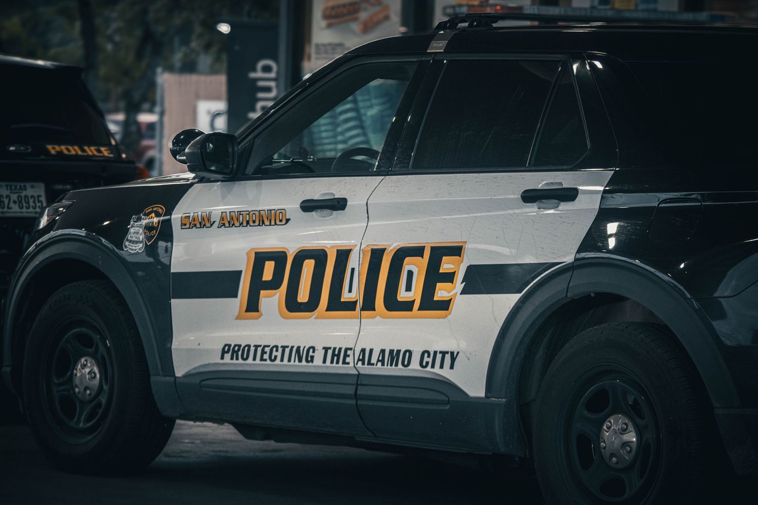 San Antonio Police Department patrol car with Protecting the Alamo City motto parked on city street.