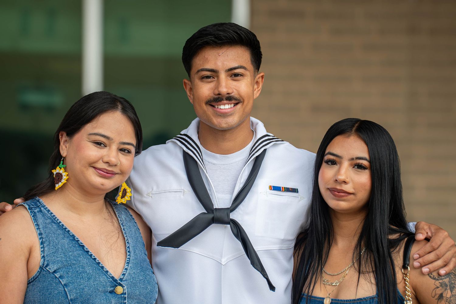 Navy sailor in dress whites smiles with two female family members at military graduation.