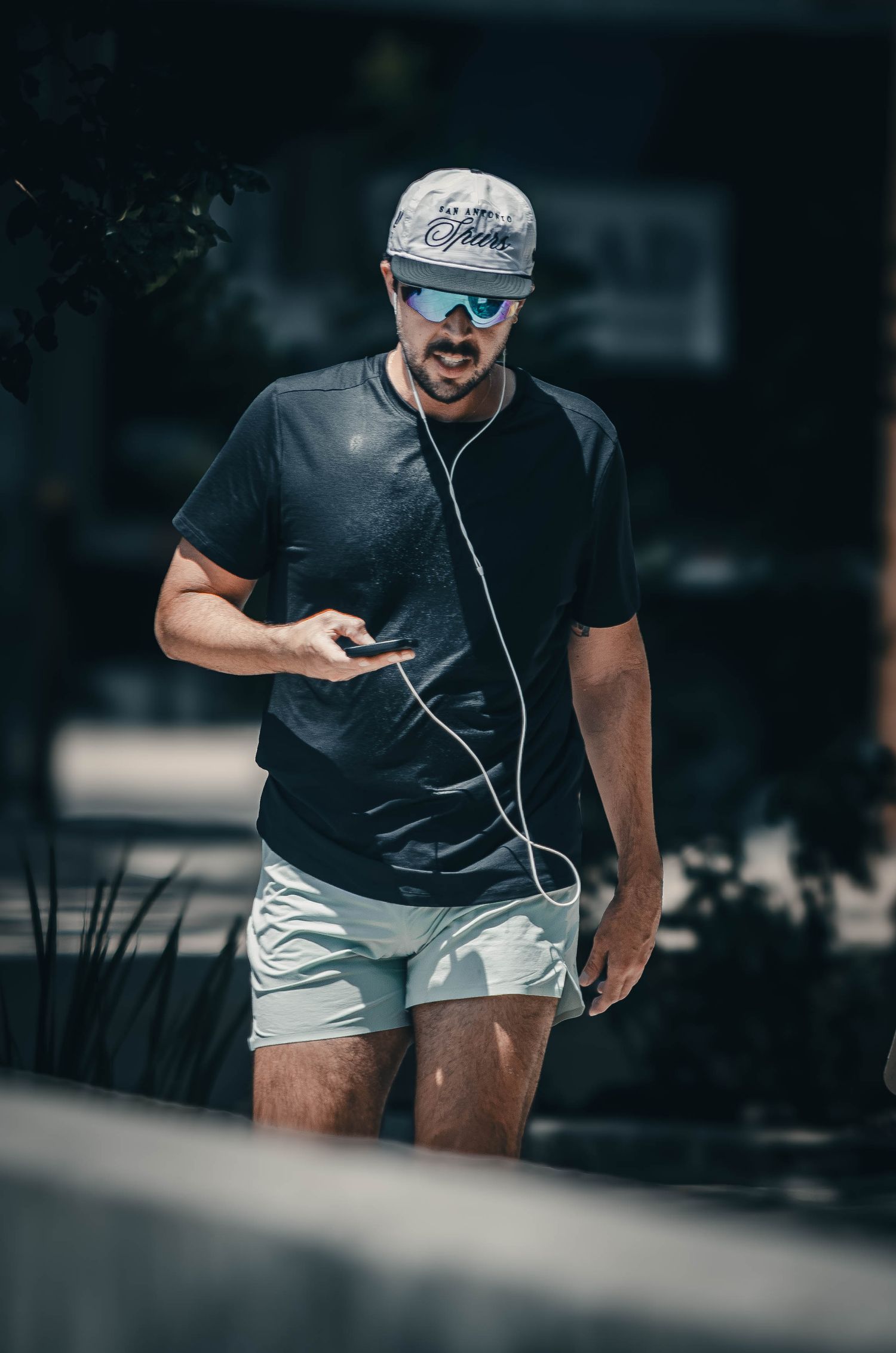 Athletic man in black shirt and shorts jogging outdoors while listening to music on earphones.