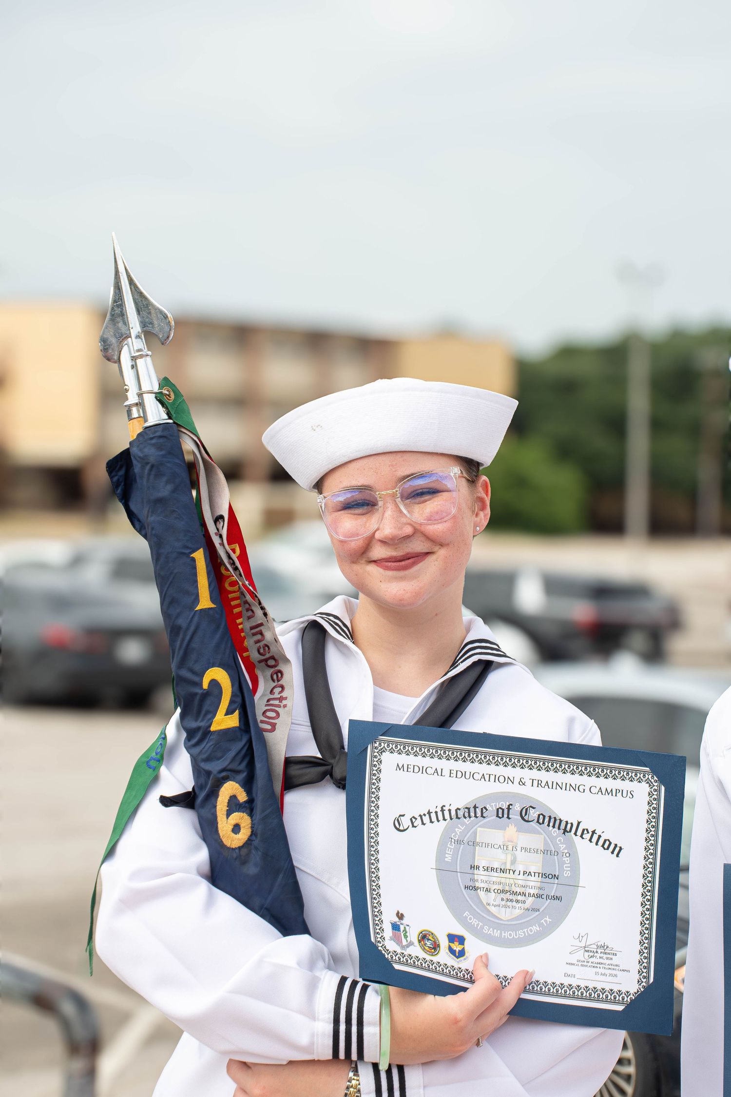 Female Navy sailor holds guidon and Certificate of Completion at METC graduation ceremony.