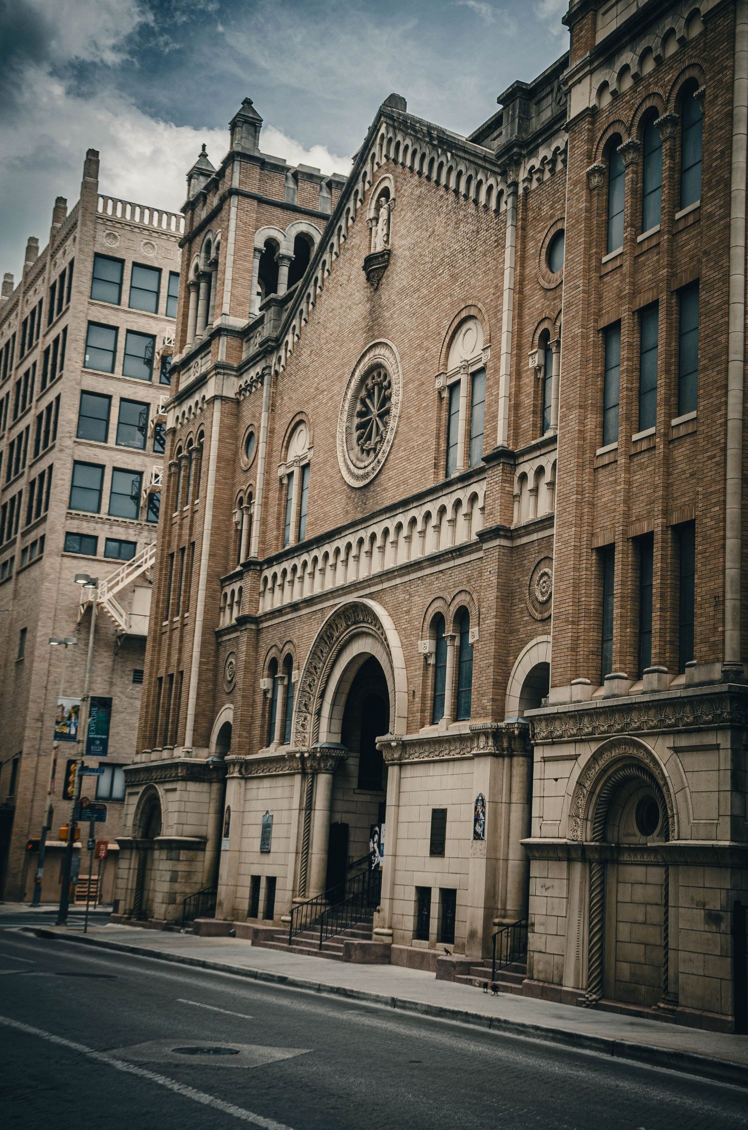 Ornate historic brick church facade with Romanesque arches and rose window on a city street.