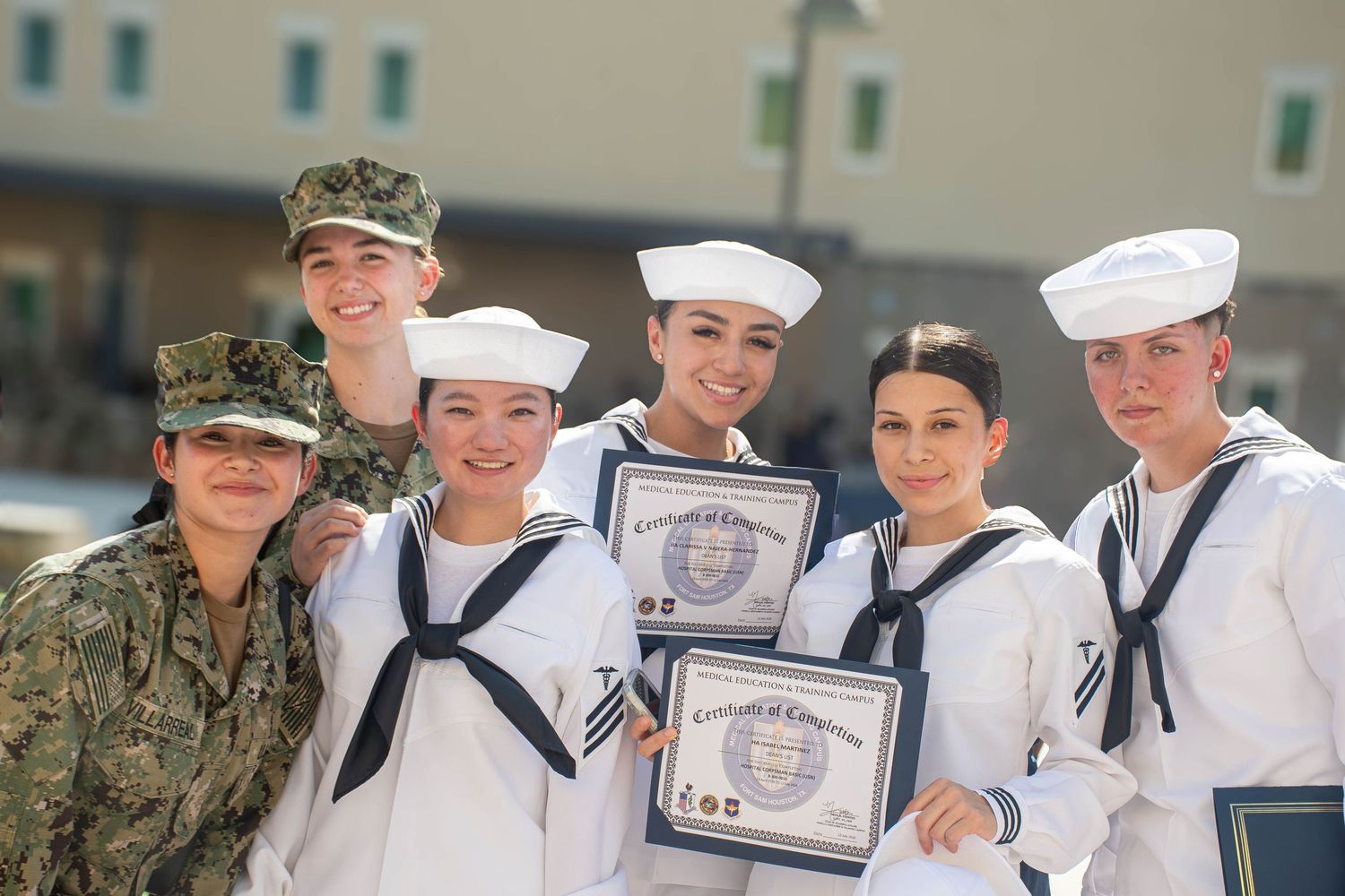 Group of Navy sailors in dress whites pose with certificates alongside uniformed military personnel.