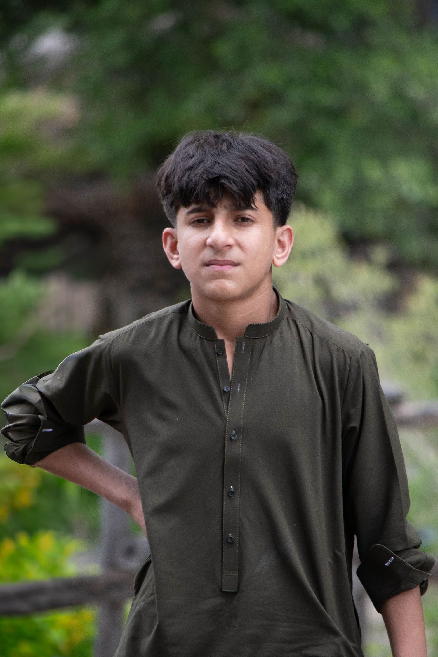 Young teenage boy in olive green traditional shalwar kameez standing outdoors in nature.