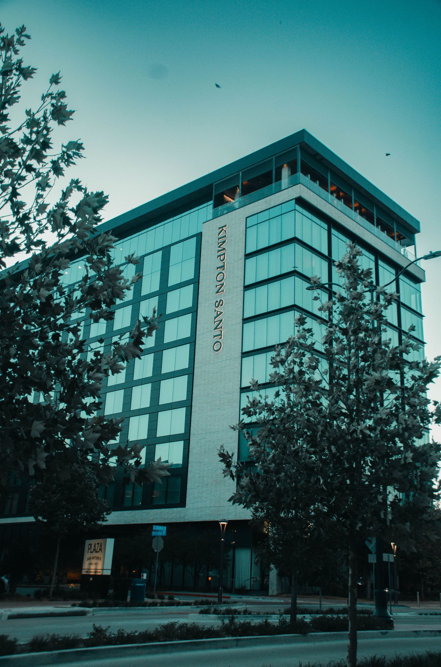 Modern Kimpton Santo hotel glass building surrounded by trees at dusk.