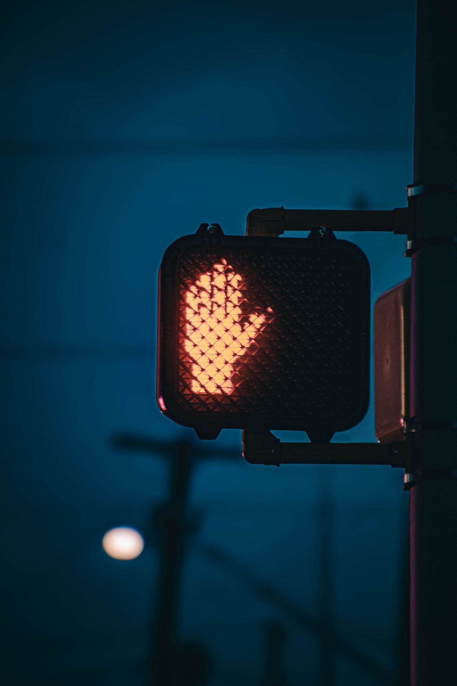 A glowing red pedestrian stop hand signal illuminated against a dark blue night sky.