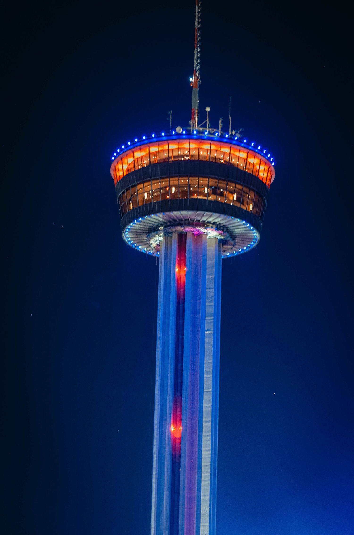 Tower of the Americas illuminated in blue and orange lights against a dark night sky in San Antonio.