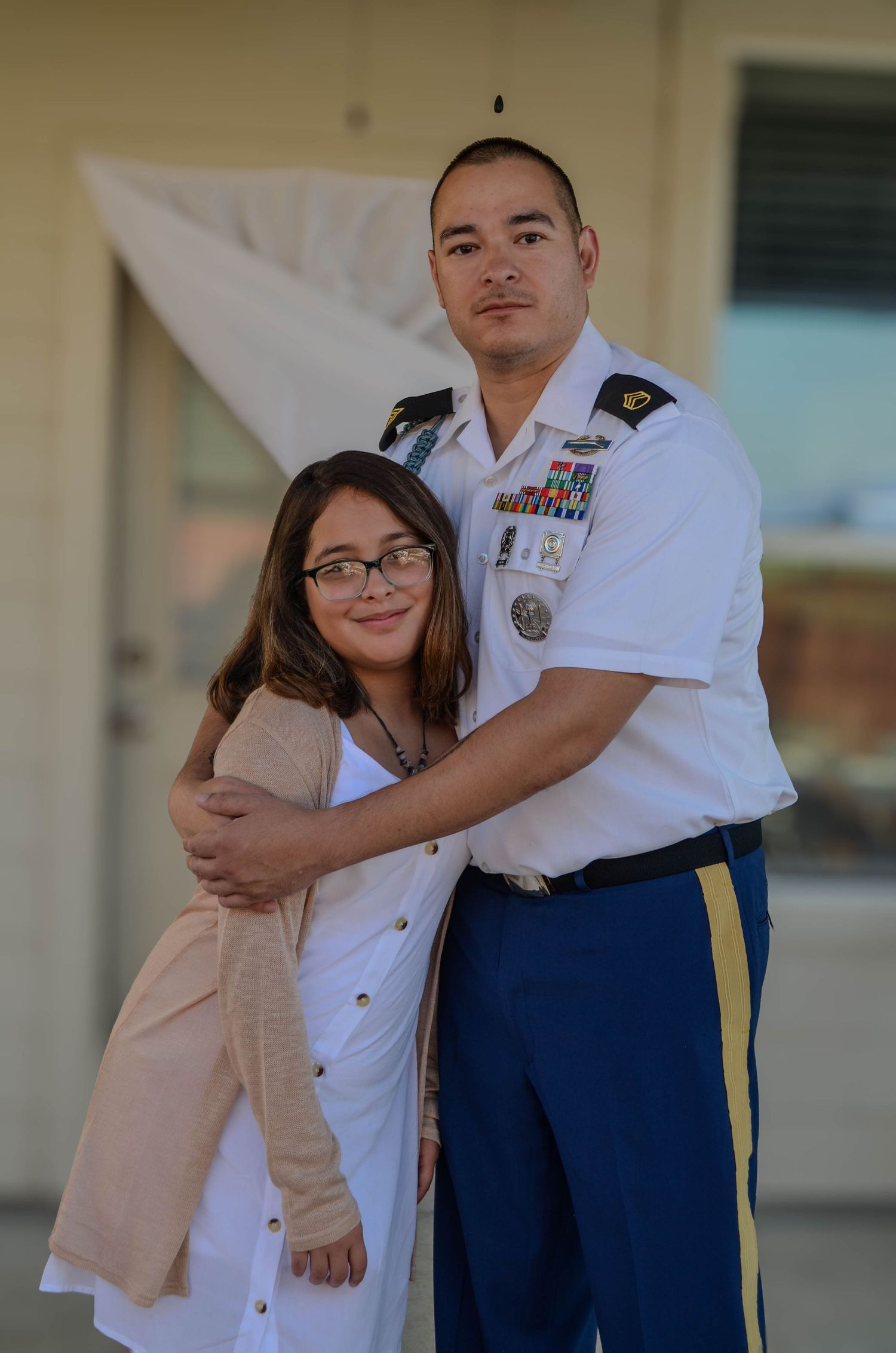 US Army soldier in dress uniform embracing a young woman outdoors.
