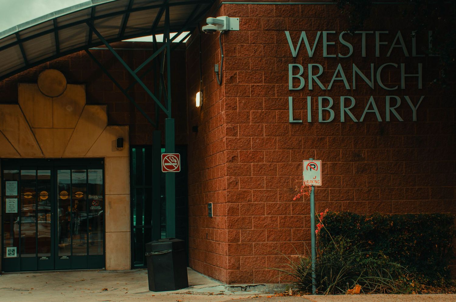 Exterior brick wall of Westfall Branch Library with green metal signage and arched entrance.