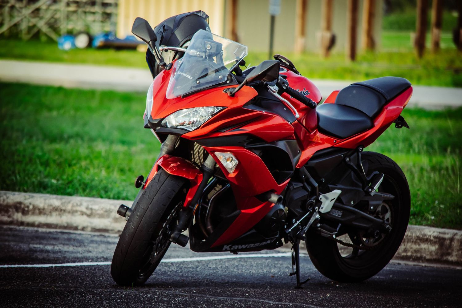 Red sport motorcycle parked on pavement with green grass background, showcasing sleek fairing and windscreen design.