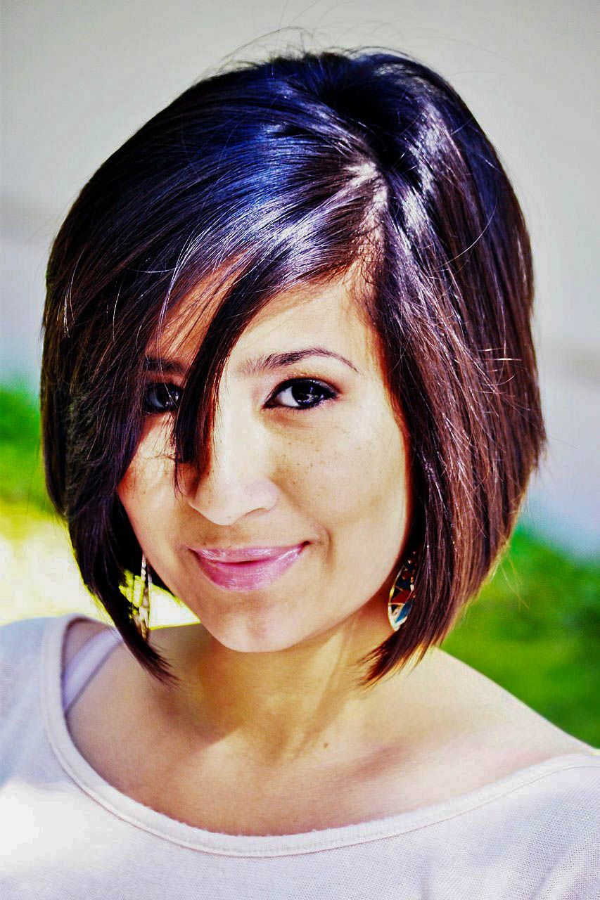 Woman with stylish dark bob haircut smiling at the camera outdoors.