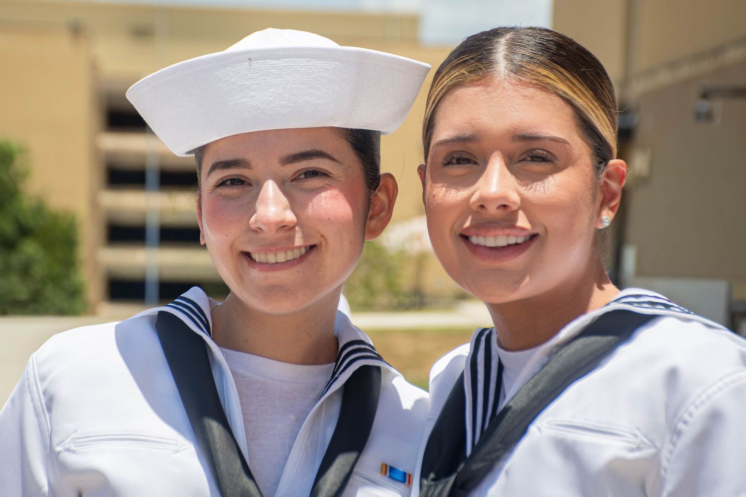 Two smiling female Navy sailors in white uniforms and hats at graduation.