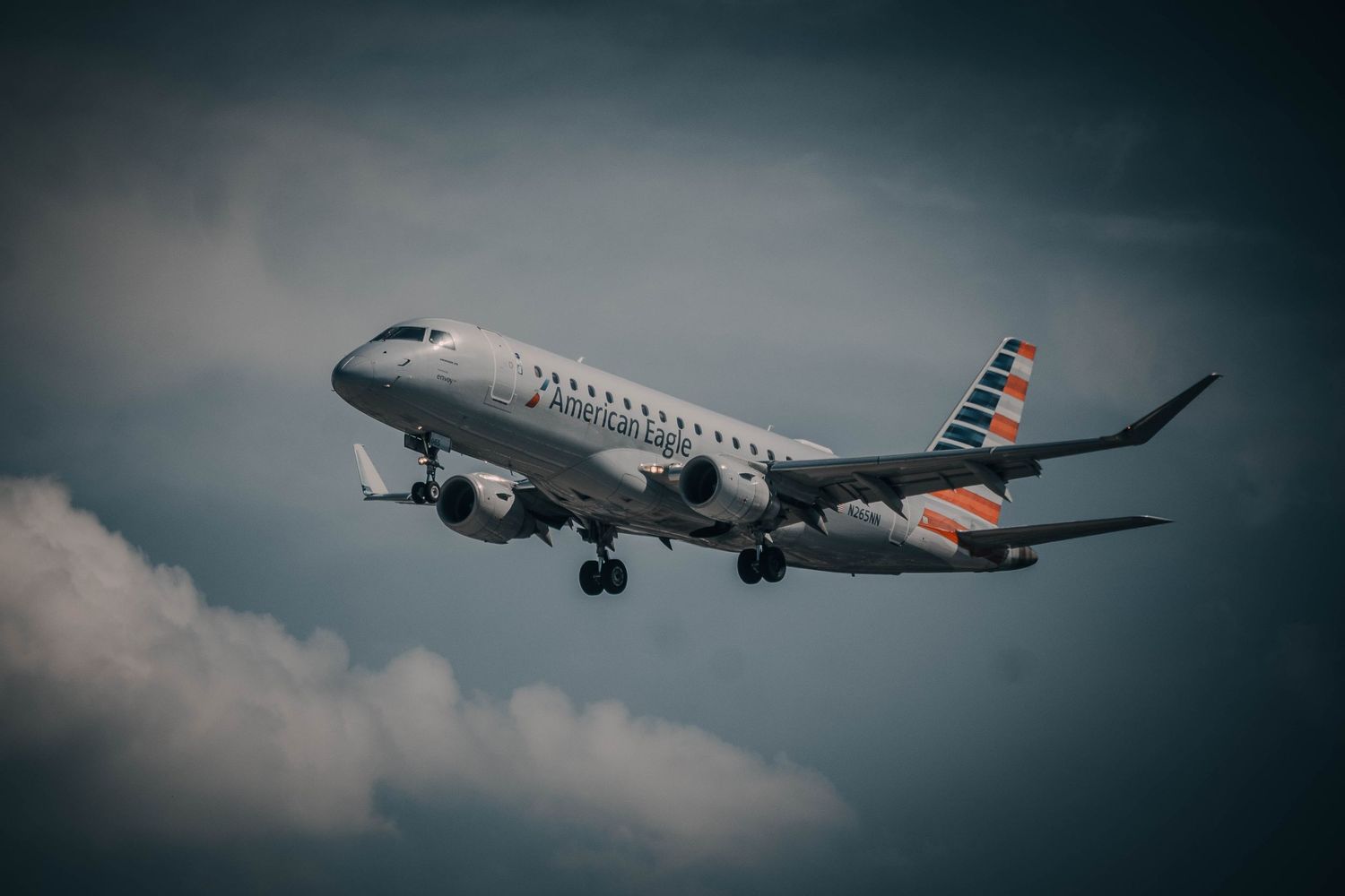 American Airlines regional jet Embraer E175 flying against cloudy sky during approach to landing.
