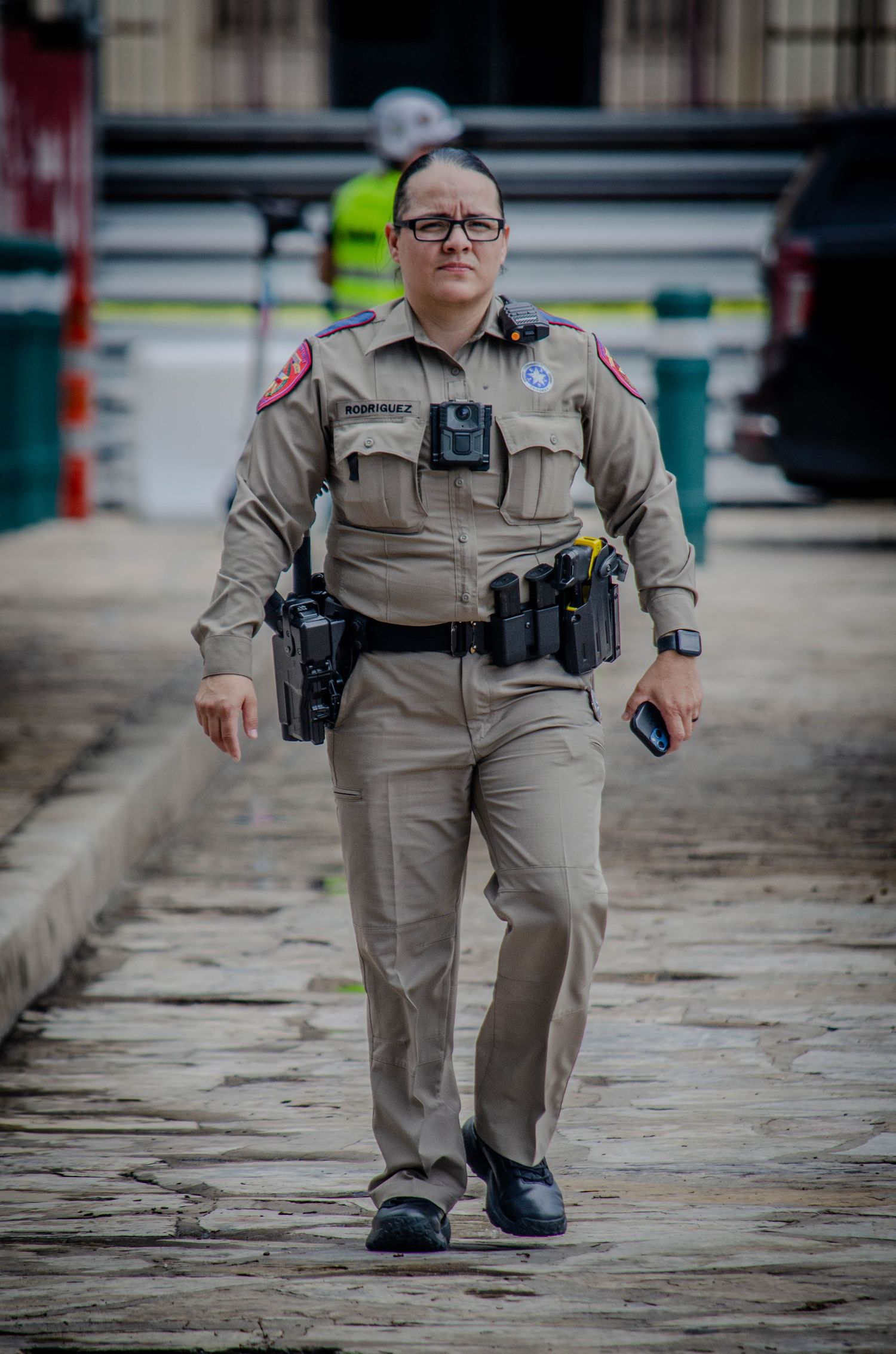 Texas law enforcement officer in tan uniform walking on a cobblestone path with full duty belt.