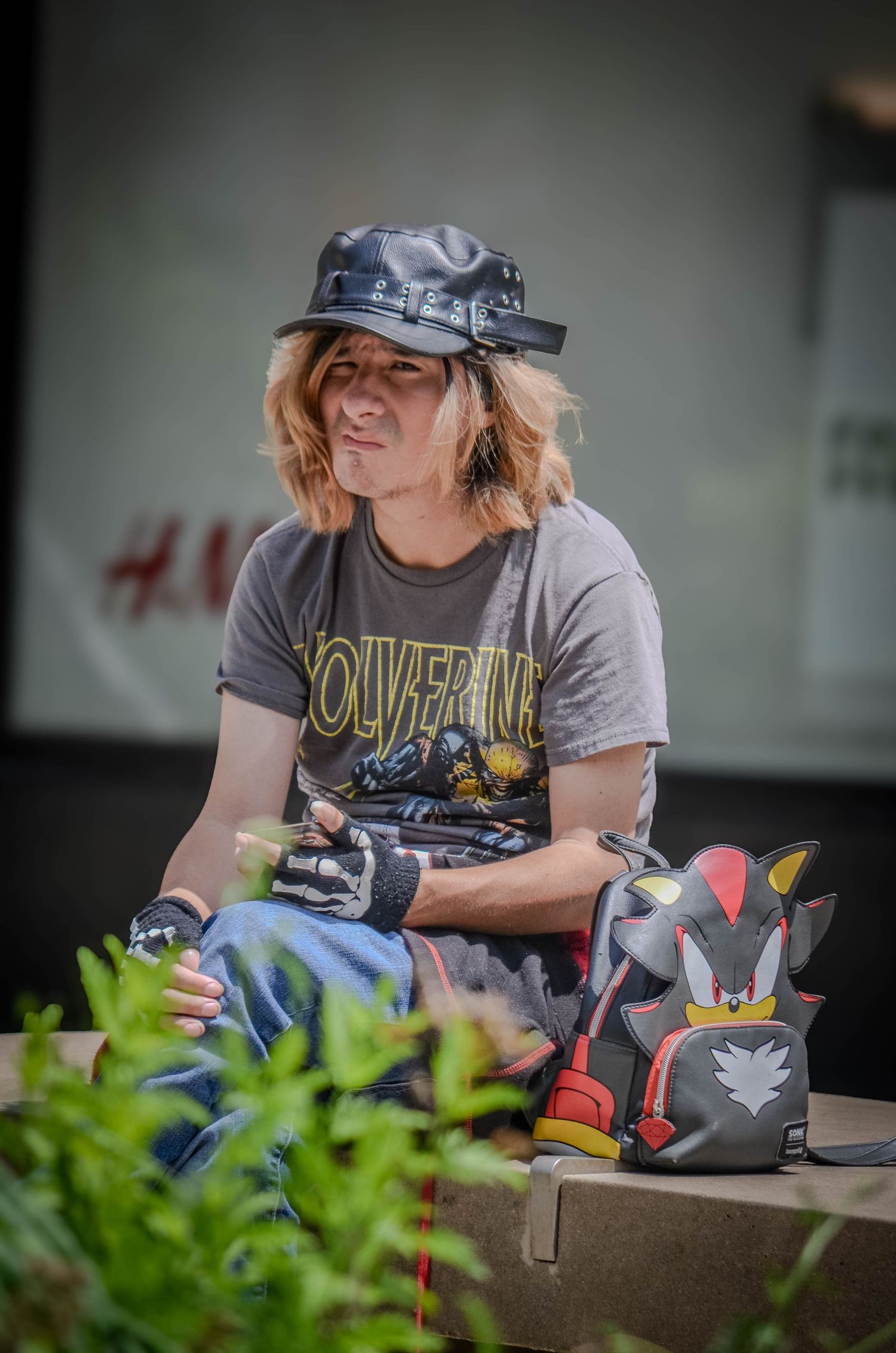 Young person in Wolverine shirt and leather hat sitting outdoors with Pokemon backpack.
