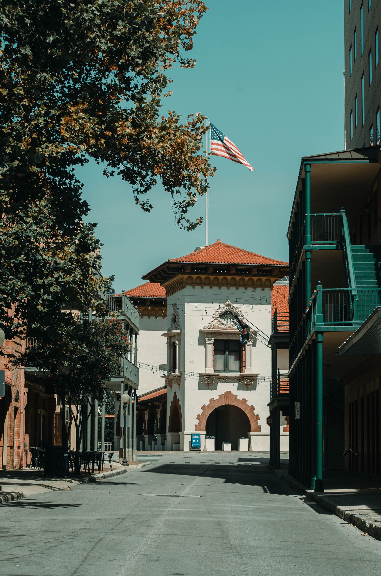 Historic building with American flag on top along a quiet street with trees and colorful architecture.