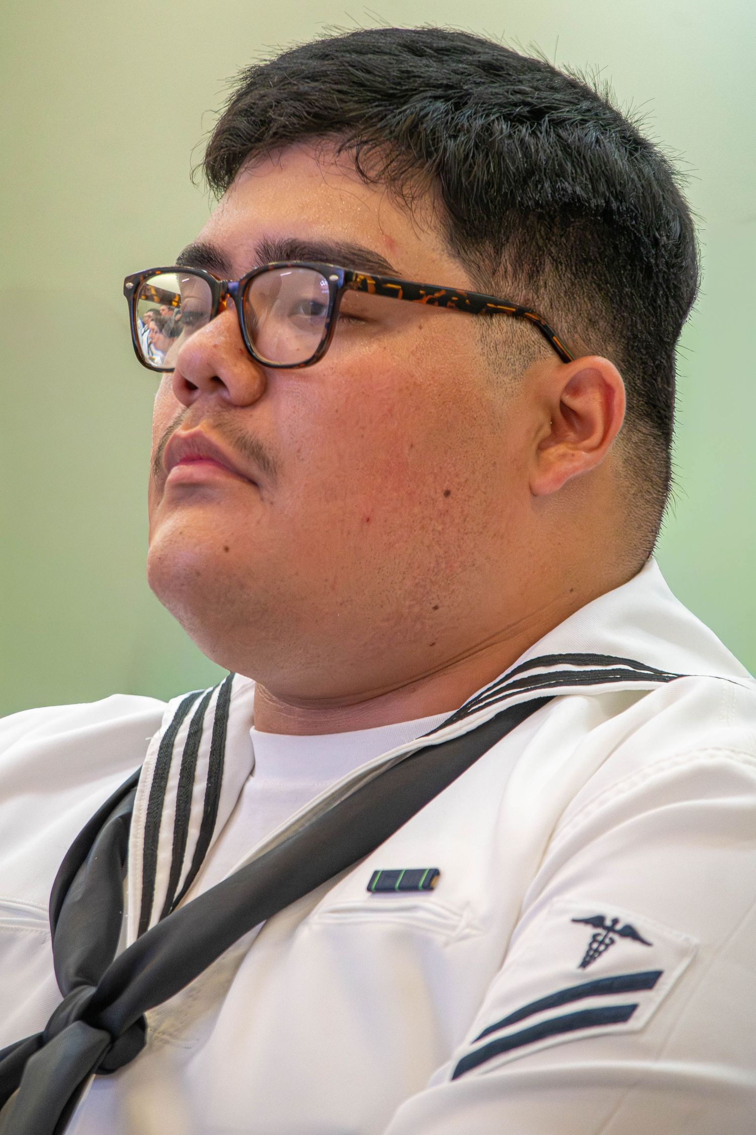 Male Navy sailor wearing glasses in white dress uniform with medical corps insignia in profile view.