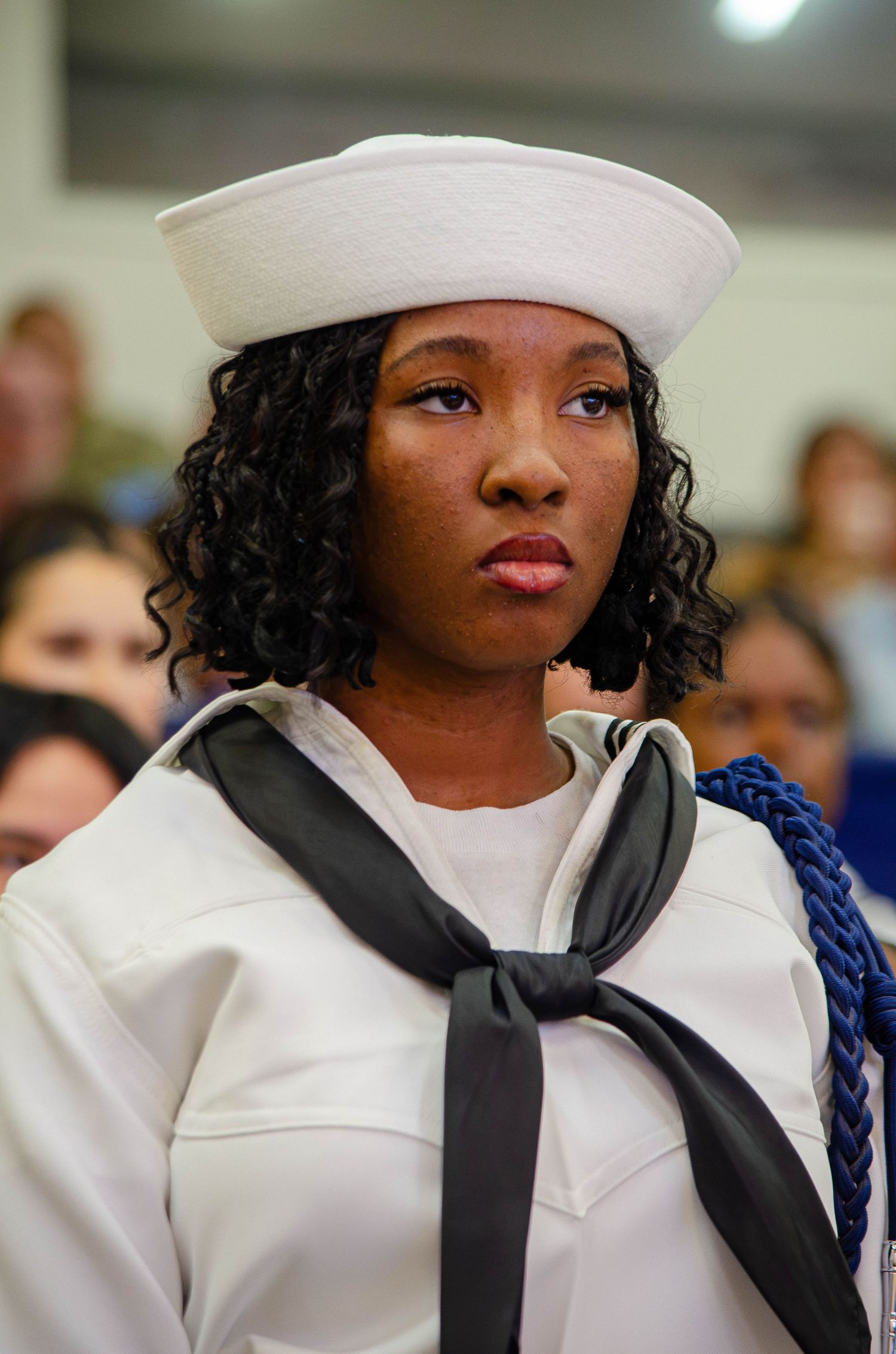 Young female Navy sailor in white dress uniform and white hat at military event.