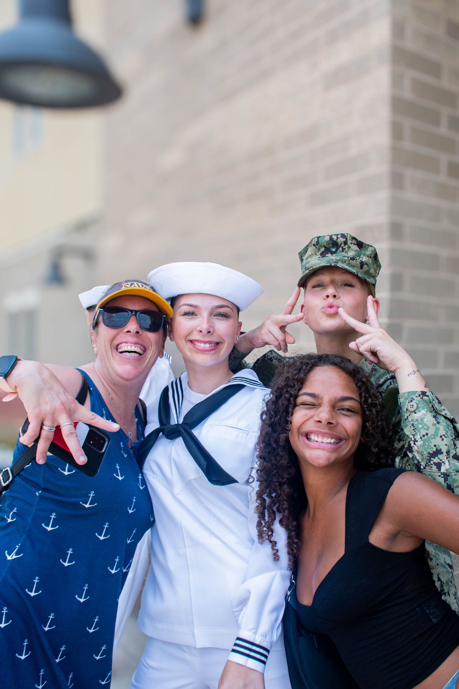 Four women including two Navy sailors smile and pose together outdoors.