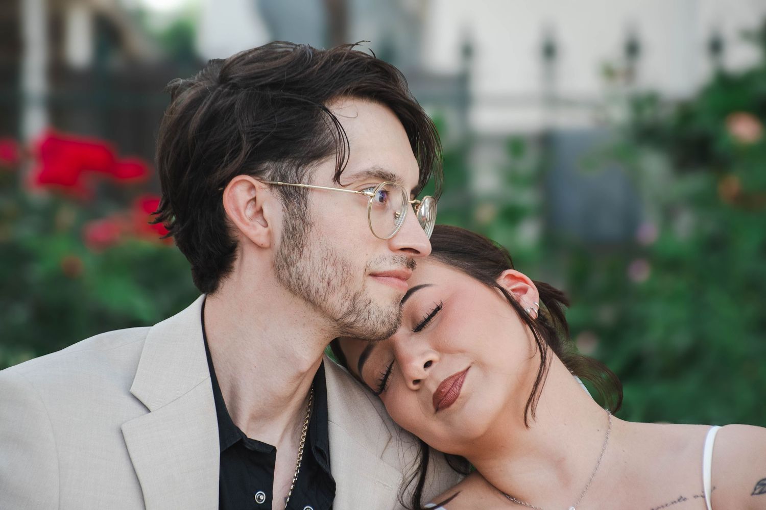 Romantic couple moment with woman resting head on mans shoulder outdoors near red roses.