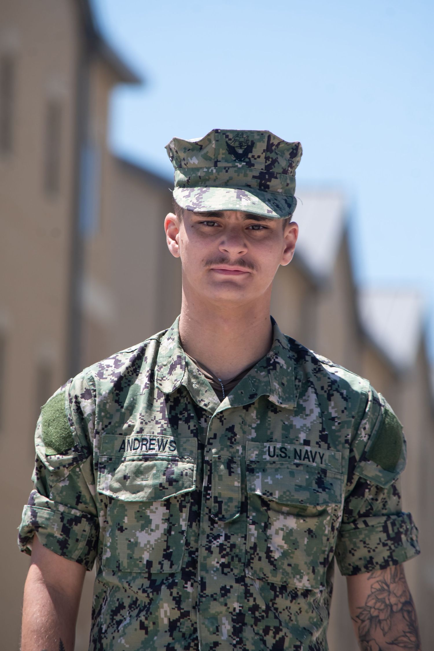 Young male US Navy sailor in digital camouflage uniform standing outdoors on a sunny day.