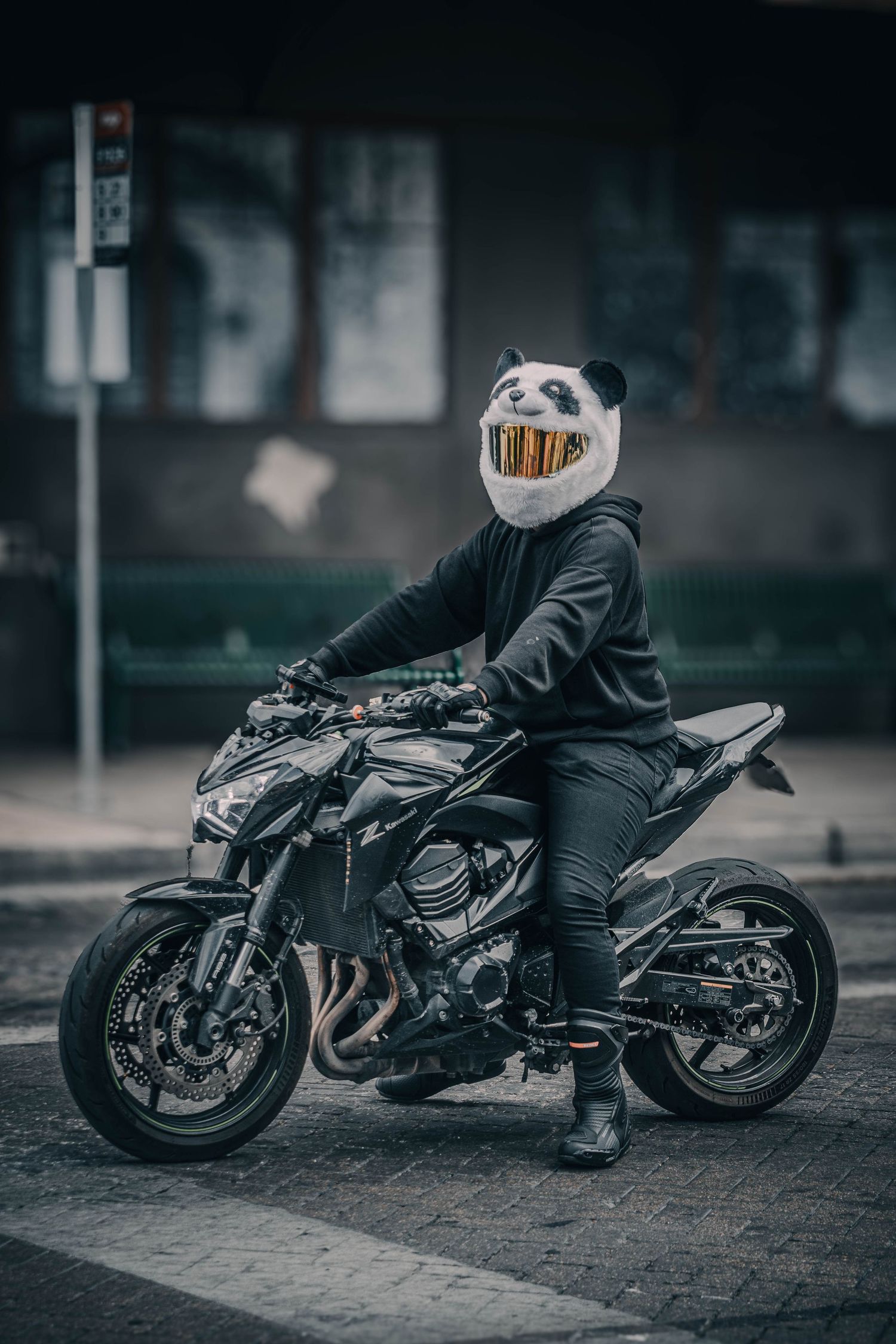 Motorcyclist wearing a panda helmet sitting on a sleek black sport motorcycle on a city street.