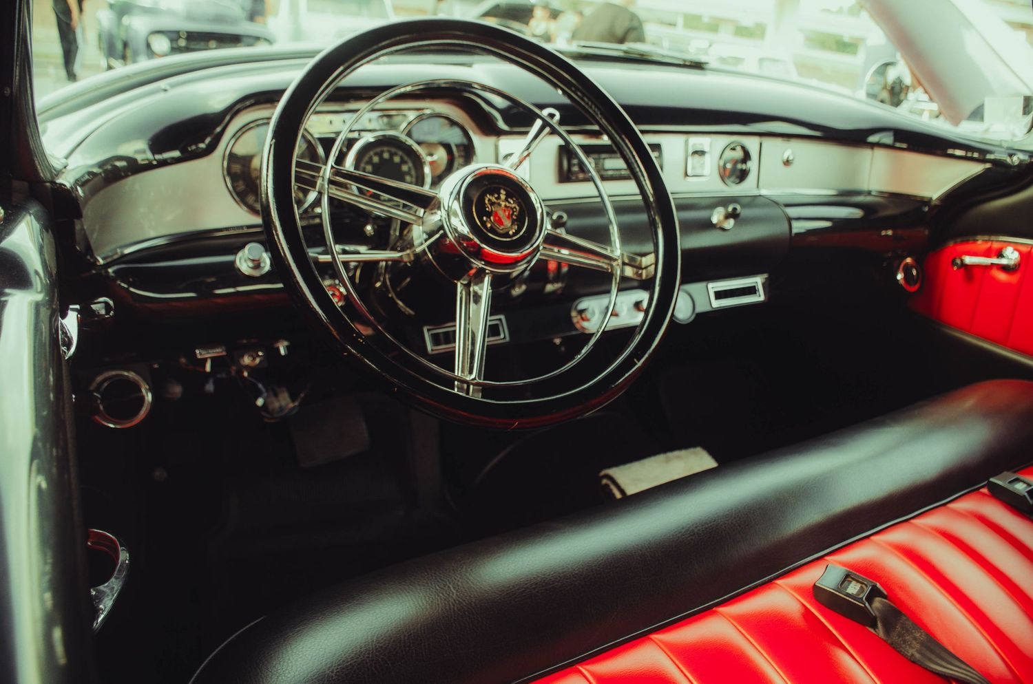 Vintage classic car interior with red leather seats, chrome steering wheel, and retro dashboard detailing.