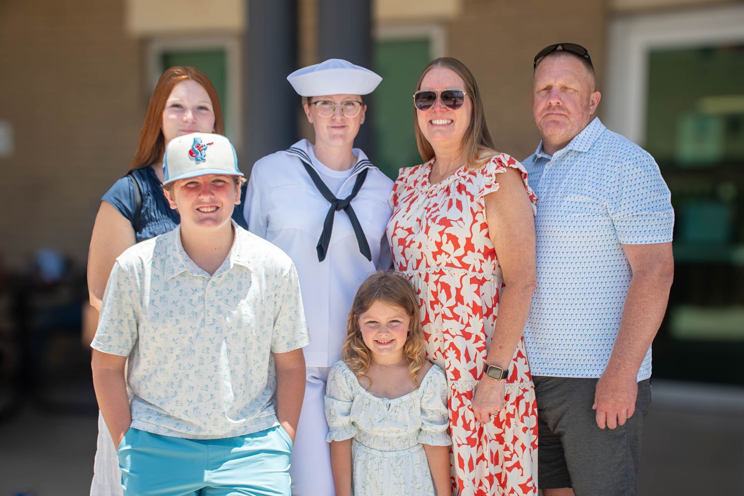 Navy recruit in dress whites poses with proud family after graduation ceremony.