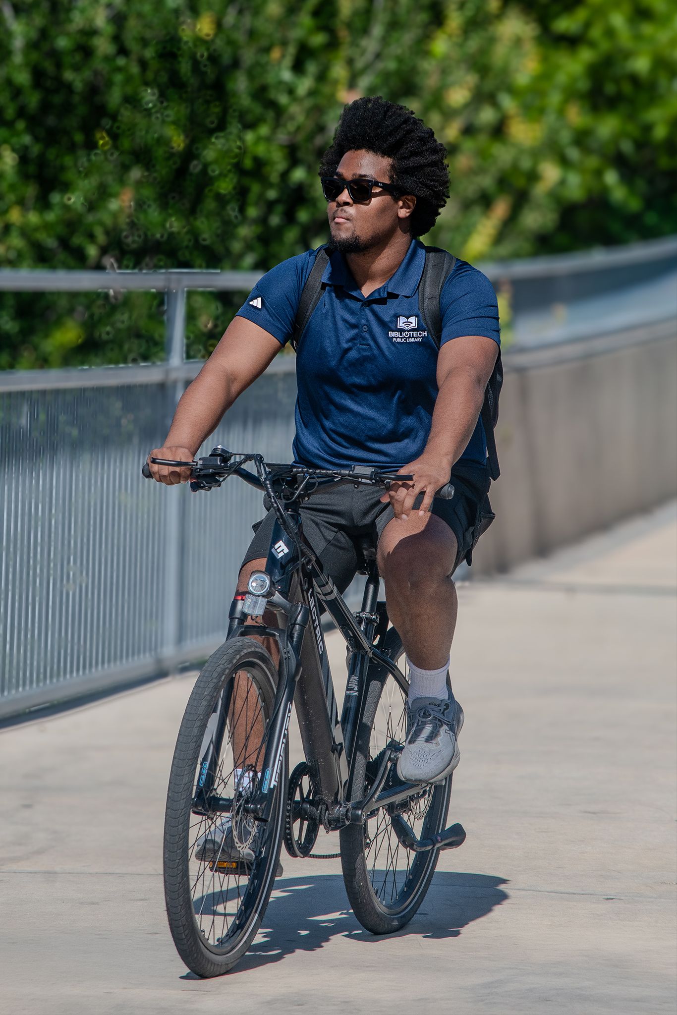 Young man with afro hair riding a mountain bike on a sunny concrete path outdoors.