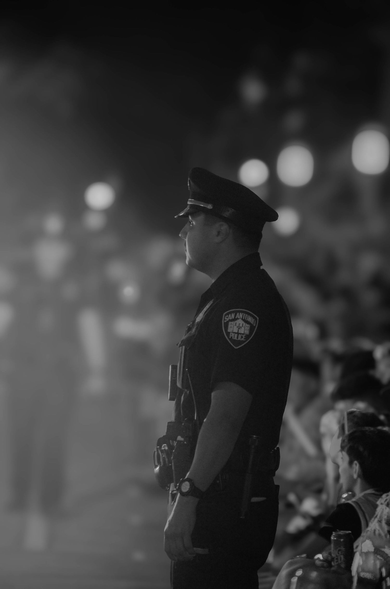 Black and white photo of San Antonio police officer standing at attention during night event.