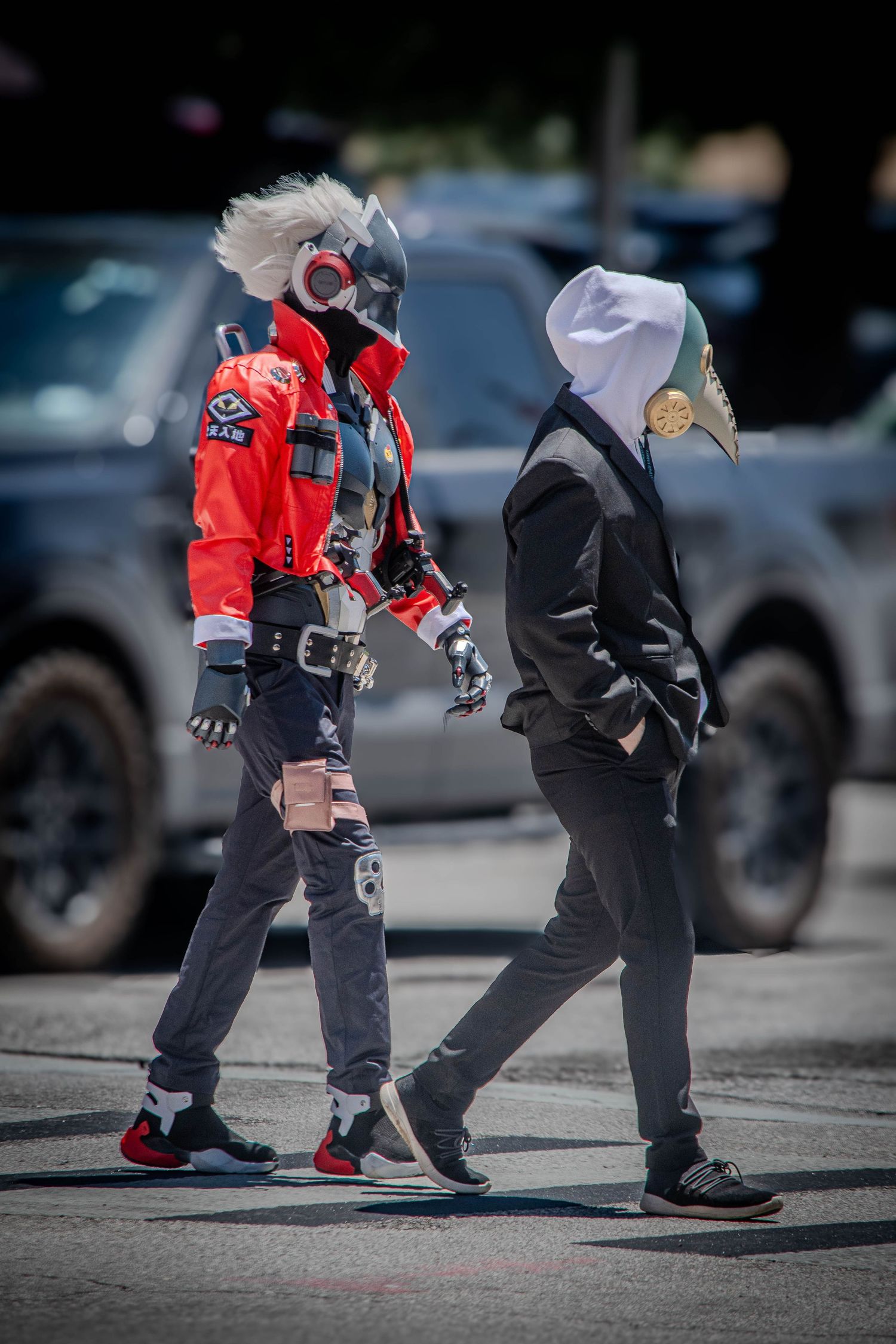 Two people in elaborate cosplay costumes walking through a sunny parking lot.