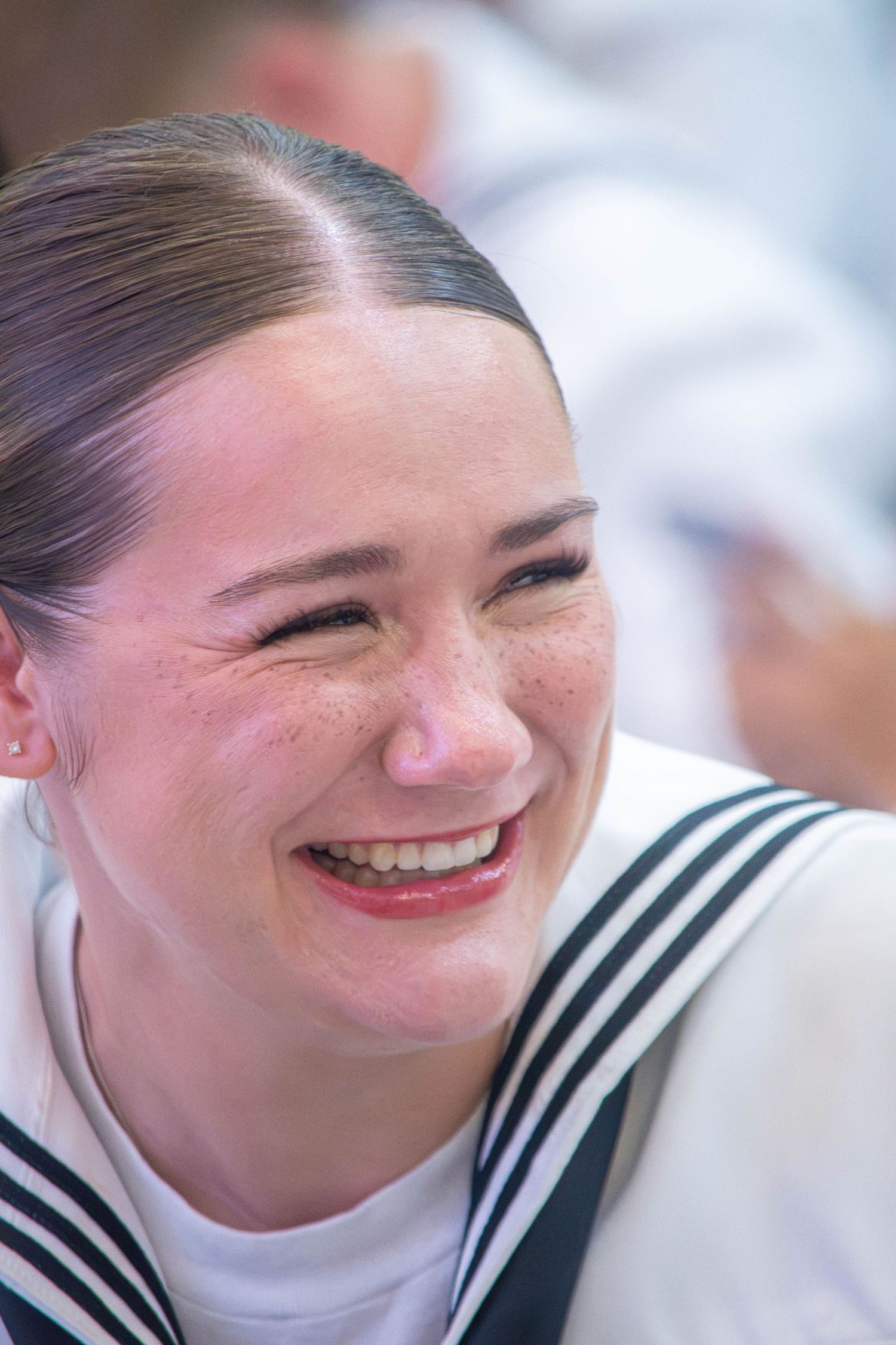 Laughing young female US Navy sailor with freckles and slicked-back hair in white uniform.