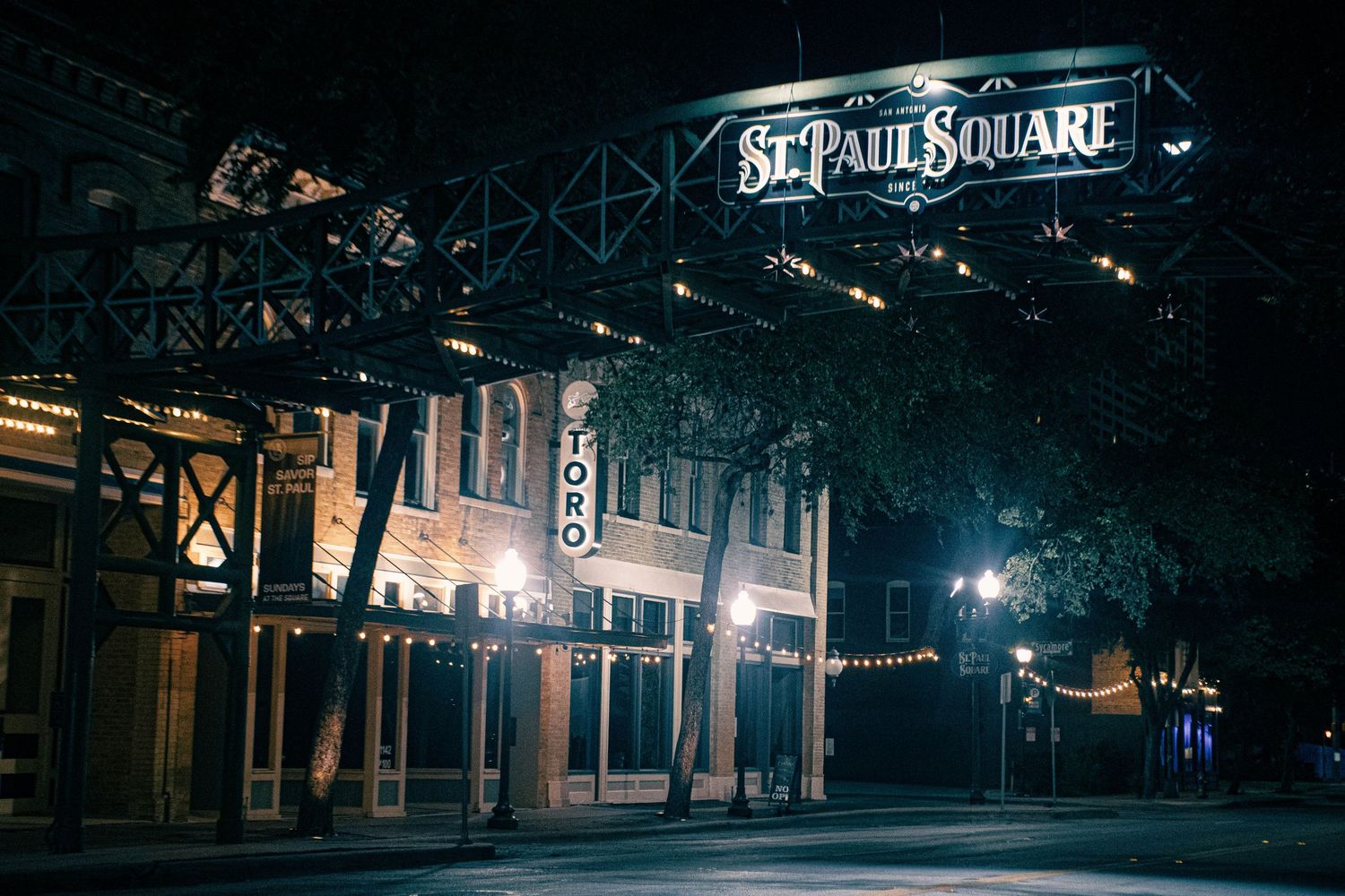Night shot of St. Paul Square entrance with illuminated signage and string lights in San Antonio.
