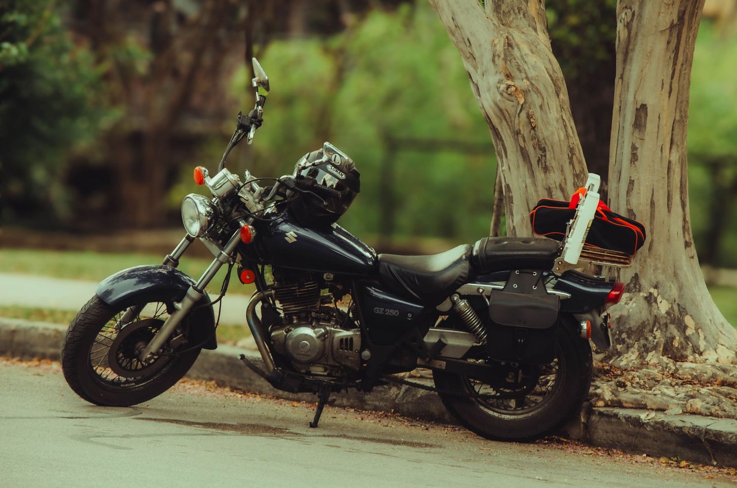 Black motorcycle parked on a sidewalk beside a large tree in a green suburban neighborhood.