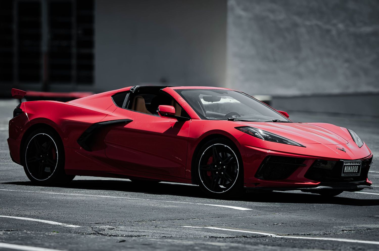 Red Chevrolet Corvette C8 mid-engine sports car parked on a gray surface, showcasing its sleek aerodynamic design.