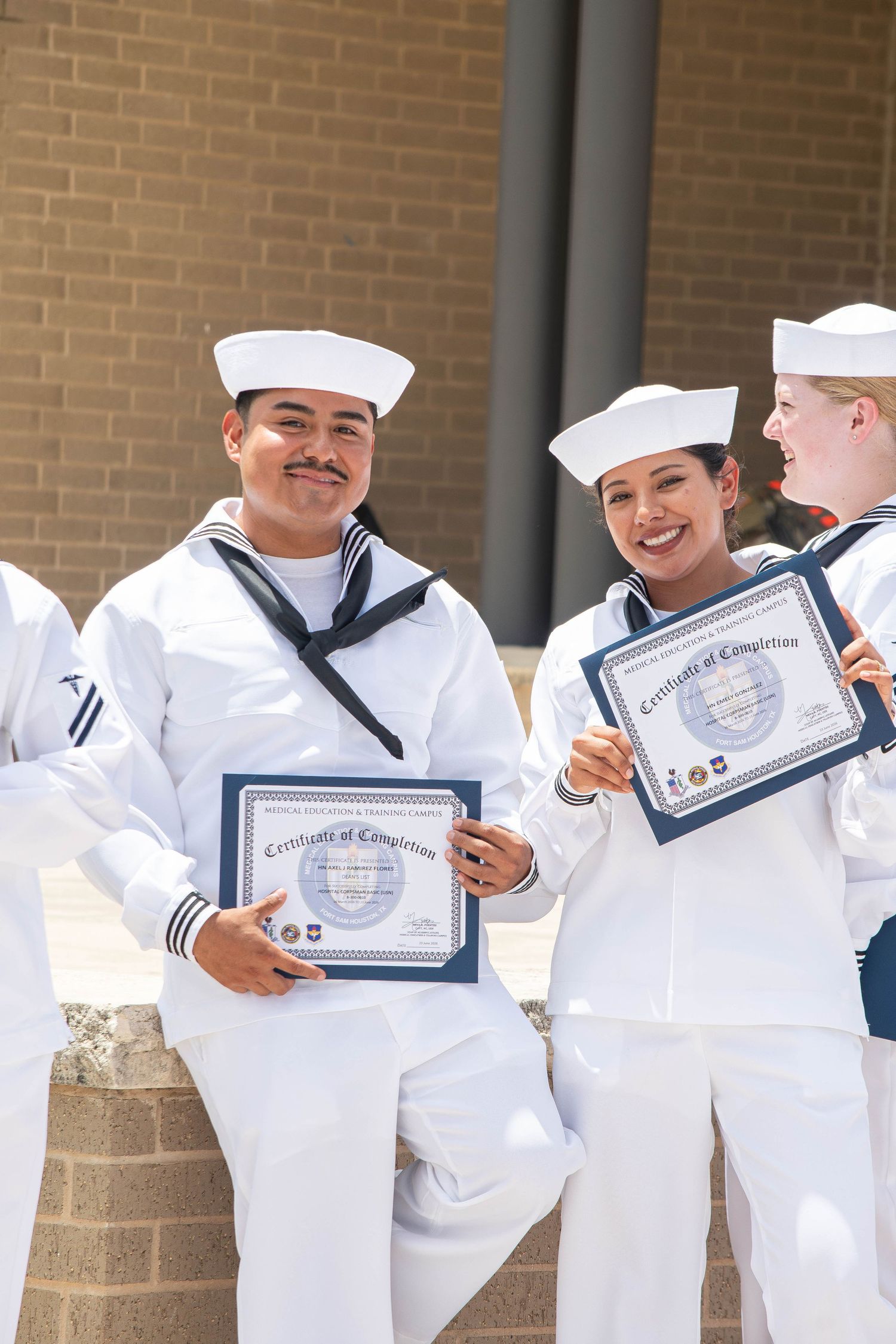 US Navy sailors in white dress uniforms proudly holding Certificates of Completion outdoors.