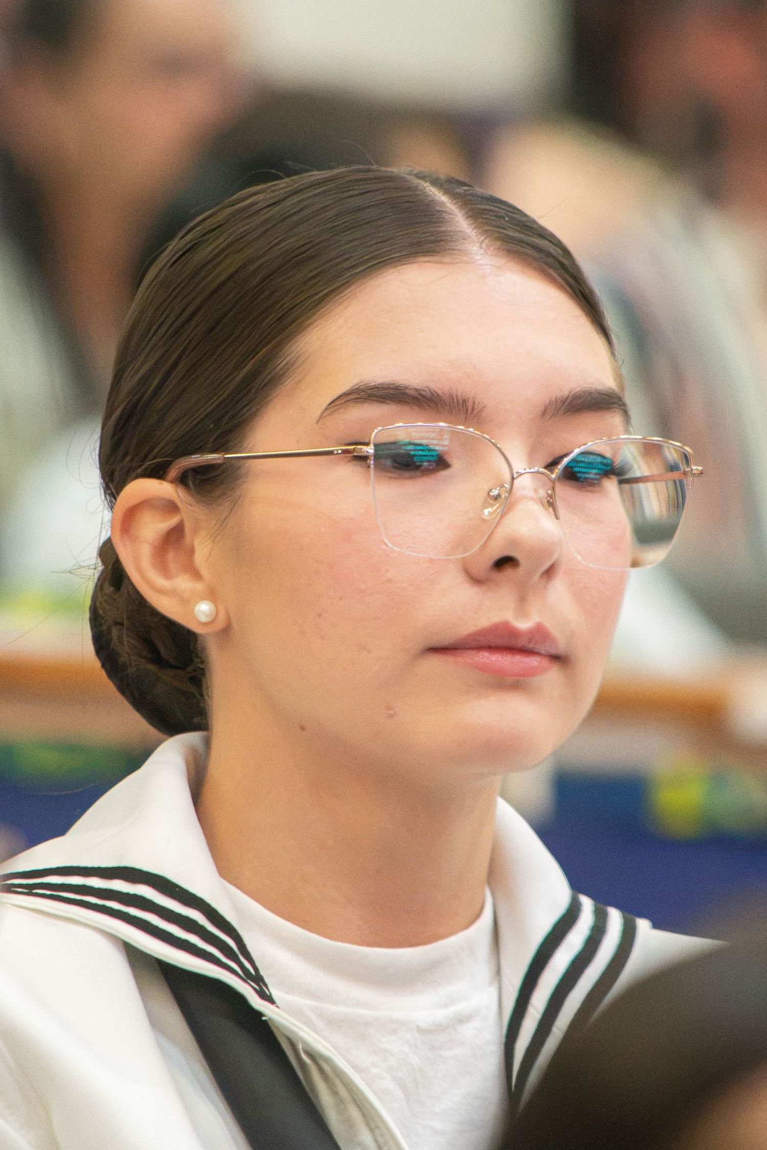 Female Navy sailor with braided bun and rimless glasses in white uniform attends military ceremony.