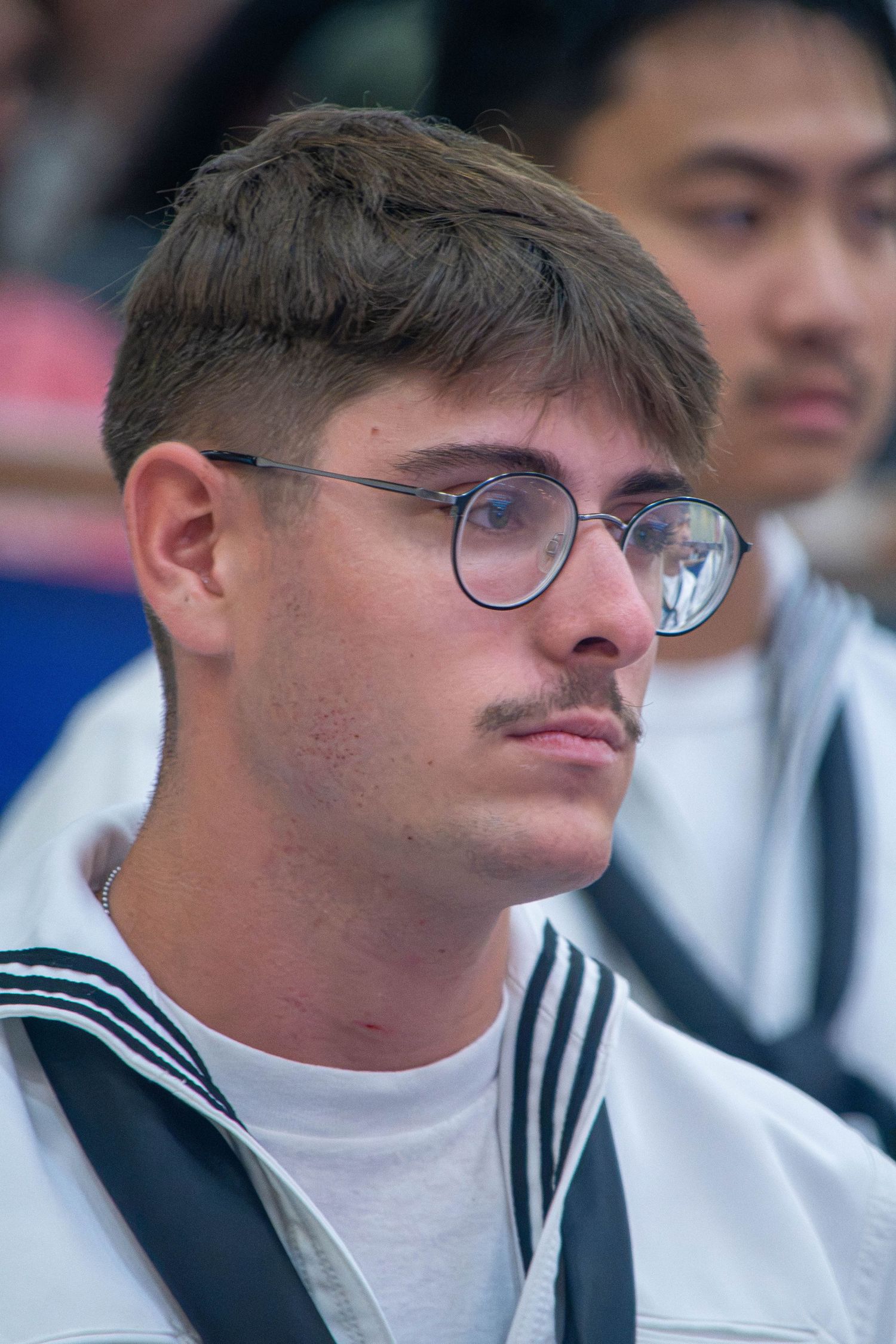 Young male US Navy sailor wearing round glasses and white dress uniform.