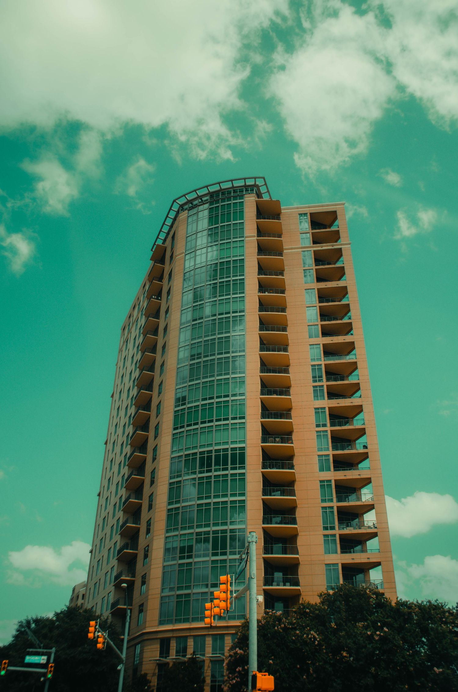 Tall residential glass and brick high-rise tower under a green cloudy sky.