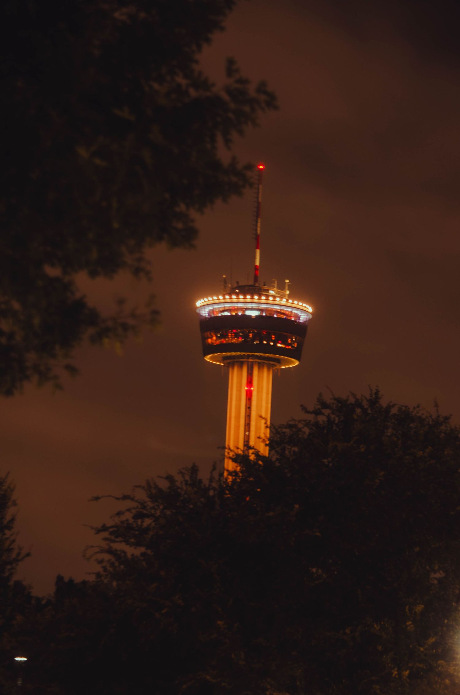 Tower of the Americas observation tower lit up with colorful lights against a dark night sky.